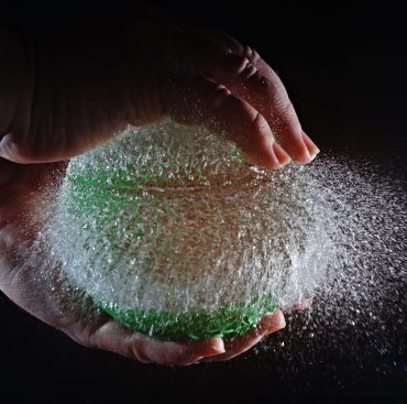 A slow motion shot of a person popping a balloon filled with water and a black background