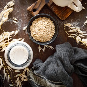 Vegan oat milk in glass bottle and ingredients for cooking. Healthy vegetarian non-dairy drink or beverage. Alternative milk