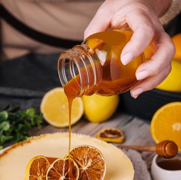 woman pouring caramel on orange cheesecake